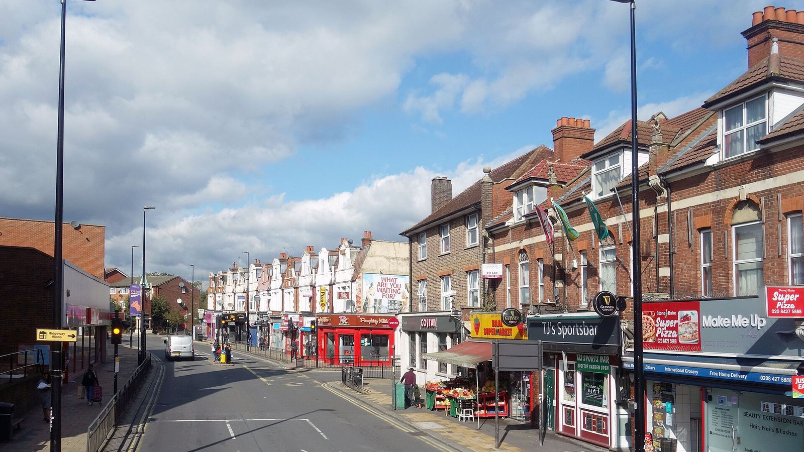 A British high street lined with independent shopfronts and signage under a cloudy sky