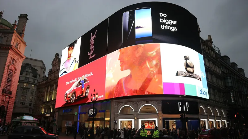 Illuminated advertising screens dominating Piccadilly Circus at dusk, with traffic and crowds below